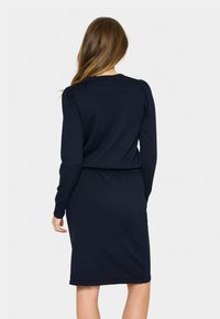Robe en tricot bleu marine à manches longues, avec une taille ajustée et une silhouette droite, présentant un tissu texturé et des poignets côtelés.