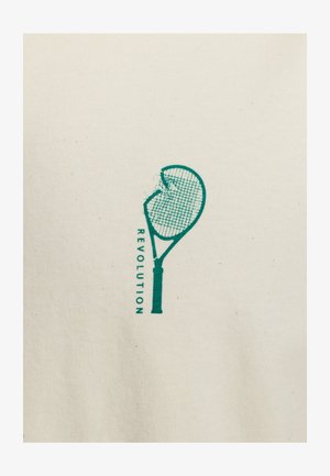 T-shirt en coton beige avec un graphisme vert d'une raquette de tennis cassée accompagnée du mot "RÉVOLUTION" imprimé verticalement.