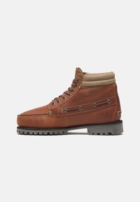 Bottine en cuir marron avec col beige rembourré, œillets métalliques, détails cousus et semelle noire épaisse à crampons profonds.