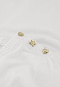 Witte gebreide trui met gouden decoratieve knopen in de vorm van een bloem, ster en hart, met een gladde textuur en eenvoudig ontwerp.