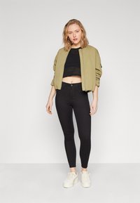 Olivově zelená bombérka, černý zkrácený pletený top a černé skinny džíny. Bílá tenisky dotvářejí outfit. Jednoduchý, ležérní design.