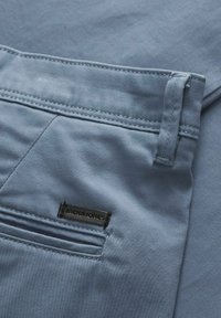 Gros plan d’un pantalon bleu clair montrant la boucle de ceinture, la poche arrière, les coutures et une étiquette noire avec le nom de la marque Jack & Jones.