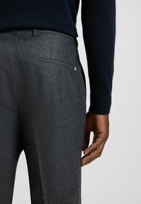 Tailored wool trousers in dark grey with a subtle check pattern, featuring a sleek design, back pocket, and a rectangular logo accent.