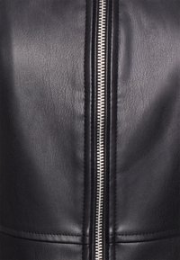 Giubbotto di pelle nera con una zip argento prominente, superficie lavorata e dettagli delle cuciture lungo i lati.