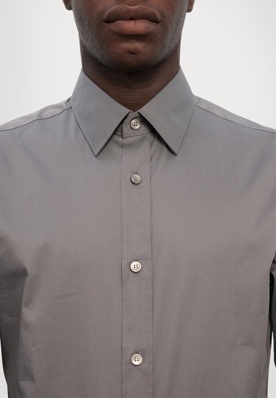 Chemise grise à col classique, avec huit boutons et un tissu lisse et texturé. Détails cousus le long des coutures.