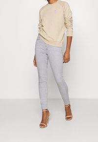 Felpa beige con scollo rotondo e polsini a costine, abbinata a jeans skinny grigi chiari e décolleté nude con cinturini.