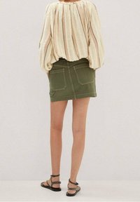 Lys, stribet bluse med voluminøse ærmer, parret med en tætsiddende grøn denimskørt med lommer og kantdetaljer, suppleret med flade sandaler.