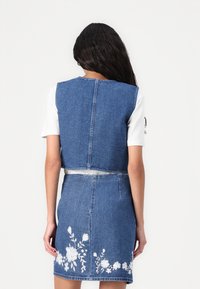 Colete de ganga com um design cropped, apresentando uma costura nas costas, combinado com uma saia de ganga decorada com bordados florais brancos na margem.