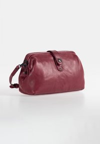Red leather clutch bag with a rounded shape, a zippered top, and a detachable wrist strap. Features flat accents and smooth texture.