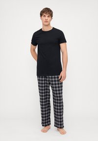 Črna bombažna majica v kombinaciji s karirastimi pižama hlačami v odtenkih mornarsko modre, bele in sive. Hlače imajo elastičen pas in ohlapen kroj.