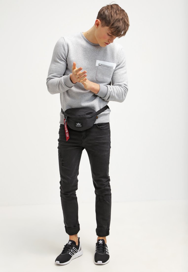 Gray sweatshirt with a chest pocket, black fanny pack, distressed black jeans, and black sneakers with white accents. Simple design and materials.
