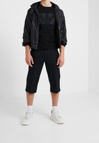 Svart lättviktsjacka med vit söm, svart logotyp t-shirt, knälånga svarta shorts och vita sneakers med diskreta accenter.