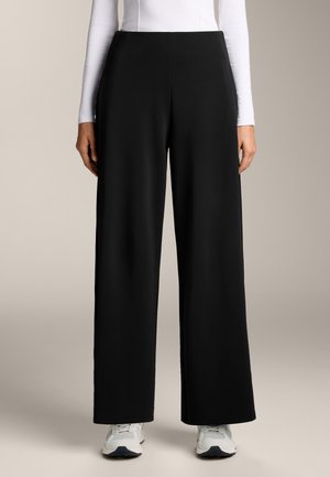 Black wide-leg pants made of soft fabric, featuring a high waistband and side pockets, paired with white sneakers for contrast.