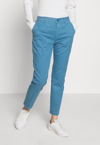 Ljusblå bomullsbyxor med slim fit, med framfickor, knappstängning och uppvikta byxben, kombinerat med vita sneakers.