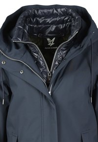 Marineblau wasserfeste Jacke mit Kapuze, metallischen Reißverschlüssen und einem gesteppten Innenfutter. Verfügt über Druckknöpfe und Kordeln am Kragen.