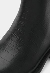 Černá kotníková bota s texturovaným vzorem krokodýlí kůže na hladkém koženém povrchu.