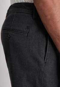 Ciemnoszare spodnie z fakturowanej tkaniny, z tylną kieszenią zapinaną na guzik oraz subtelnym logo w pobliżu kieszeni.