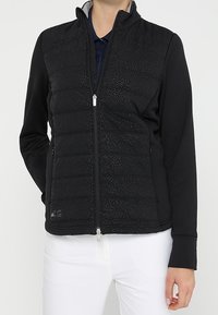 Veste noire avec une partie avant matelassée et un dos en tissu lisse. Dotée d'un col montant et de deux poches latérales zippées. Motif texturé subtil.