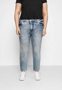 Hellblaue Denim-Jeans mit entspannter Passform, die mit Distressed-Details und Five-Pocket-Design versehen sind. Kombiniert mit weißen Sneakers.