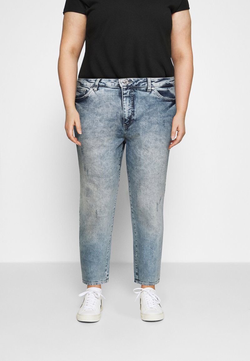 Hellblaue Denim-Jeans mit entspannter Passform, die mit Distressed-Details und Five-Pocket-Design versehen sind. Kombiniert mit weißen Sneakers.
