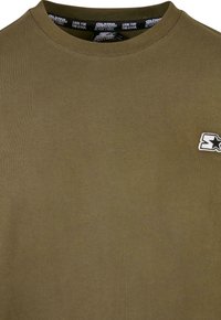 Olivenfarget bomulls T-skjorte med ribbestrikket rund hals og en liten hvit brodert logo med en stjerne på brystet.