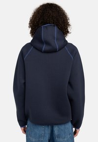 Dark navy hoodie with a hood, contrasting blue stitching, and a relaxed fit. Smooth texture with ribbed cuffs and waist.