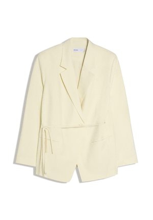 Dlhý krémový blejzer s golierom s klopou, prednými vreckami a detailom so zaväzovaním na boku, zobrazený na bielom pozadí.