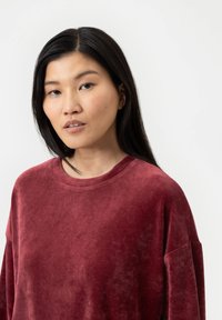 Bordeaux velours sweatshirt met een ronde halslijn, verlaagde schouders en een zachte, gladde textuur. Eenvoudig ontwerp zonder zichtbare patronen of hardware.