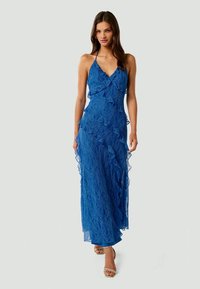 Robe maxi en dentelle bleue avec des couches froncées, décolleté en V et bretelles spaghetti, présentant une texture fluide et transparente ainsi qu'une silhouette ajustée.