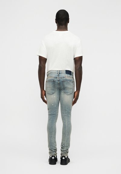 Ξεθωριασμένο μπλε τζιν με στενή εφαρμογή, με φθαρμένα σημεία και λεπτομέρεια σε πίσω τσέπη, συνδυασμένο με απλό λευκό μπλουζάκι.