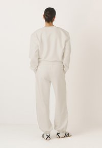 Krém színű pulóver és nadrág szett, laza fazon, puha anyag, rugalmas mandzsettákkal és derékpánttal, kontrasztos fekete és fehér lábbelivel.