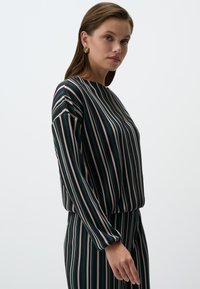 Maglietta a righe con sottili strisce verticali in verde, beige e nero. Collo rotondo, maniche lunghe e vestibilità comoda.
