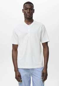 Vit kortärmad henley-skjorta med placket för tre knappar. Slät textur, avslappnad passform, kombinerad med byxor med blå ränder för kontrast.