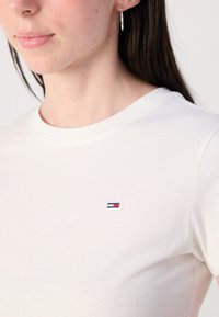 T-shirt in cotone bianco con un piccolo logo ricamato in rosso, bianco e blu sulla parte sinistra del petto. Collo rotondo e maniche corte.