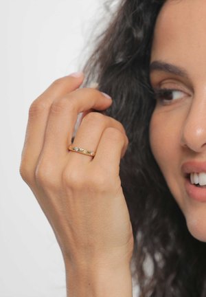 Arany gyűrű áttetsző és színes drágakövekkel, sima, polírozott felülettel. Természetes bőrtónusú kézen viselve.