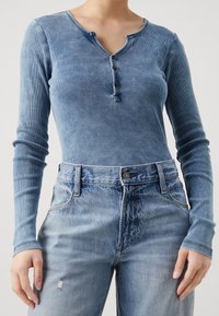 Långärmad blå ribbad topp med henley-krage och fyra knappar, kombinerad med högmidjade blekta blå jeans med slitdetaljer.