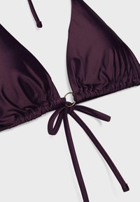 Dark purple bikini top with triangle cups, gathered edges, central metal ring, and tied adjustable straps on a light background.