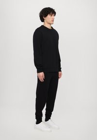 Felpa nera e pantaloni jogger realizzati in tessuto morbido. La felpa ha un collo a giro e polsini a coste, abbinati a sneakers bianche.