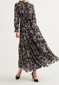 Maximekko, jossa on läpinäkyvä harmaa kangas ja musta- sekä ruusukuosiset kukat. Varustettu röyhelöpentsiellä, pitkissä hihoissa ja kerroksellisessa helmassa. Käytetään mustien korkokenkien kanssa.