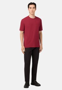 T-shirt rossa a girocollo realizzata in tessuto liscio, abbinata a pantaloni neri e sneakers nere. Design minimalista con maniche corte e vestibilità rilassata.