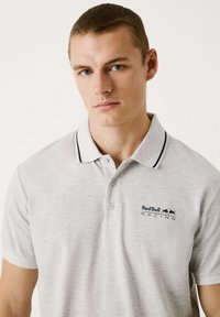 Siva polo majica s ovratnikom, dva dugmeta i mornarskim akcentima. Sadrži izvezeni logo "Red Bull Racing" na levoj strani.