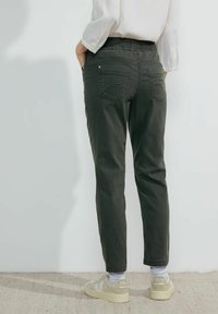 Pantalones negro de cintura elástica con bolsillos laterales, ajuste entallado y detalles de costura sutiles. Llevados con zapatillas de color claro y calcetines visibles.