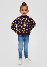 Maglione lavorato a maglia viola con motivo a cuore verde, collo rotondo e maniche lunghe, abbinato a jeans azzurri chiari e sneakers bianche.
