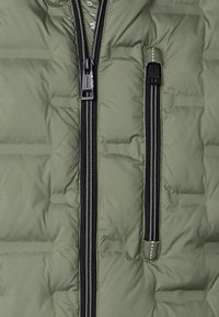 Zielona kurtka puchowa z zamkiem błyskawicznym z przodu, z czarnymi akcentami zamka, pikowaną teksturą i poziomym przeszyciem.