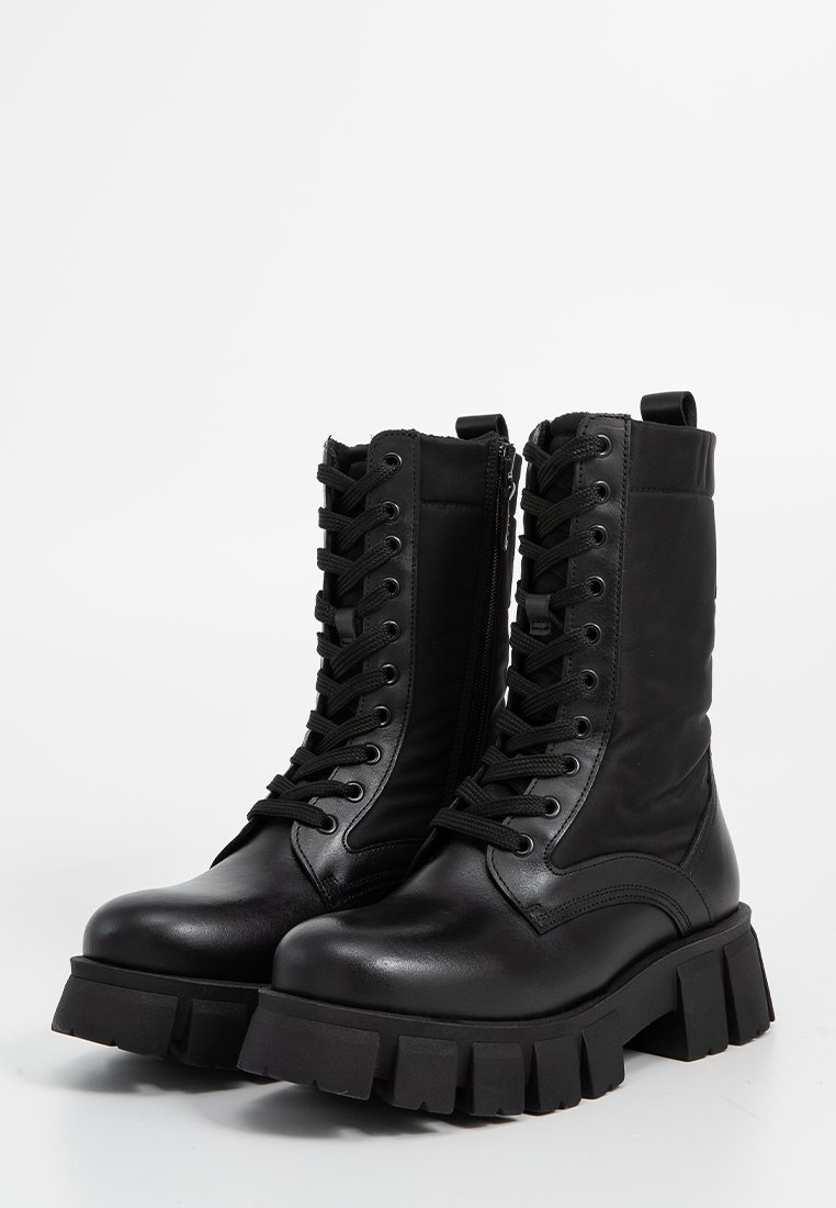 Par de botas de combate negras de cuero con cordones, suelas gruesas y cremallera lateral sobre un fondo blanco.