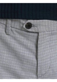 Pantalon à carreaux gris avec bouton noir, détail à rabat sous l'ourlet supérieur d'un haut côtelé noir.
