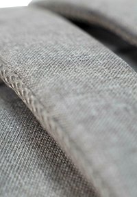 Grauer Stoff mit einer strukturierten Webart und weicher Oberfläche. Hat abgerundete Kanten und ein minimalistisches Design. Nahaufnahme, die Details hervorhebt.