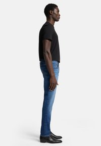 Maglietta nera, jeans blu slim-fit e stivali neri alla caviglia. L'outfit presenta un design semplice e una silhouette aderente con texture morbide.