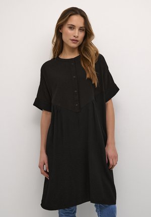 Robe noire à manches courtes, avec fermeture à boutons et un motif texturé en losanges. La robe a une coupe ample et tombe au milieu des cuisses.