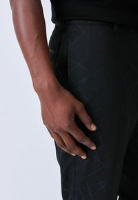 Black tailored pants with a subtle geometric pattern, textured fabric, and a slim fit, showcasing a side pocket and belt loops.